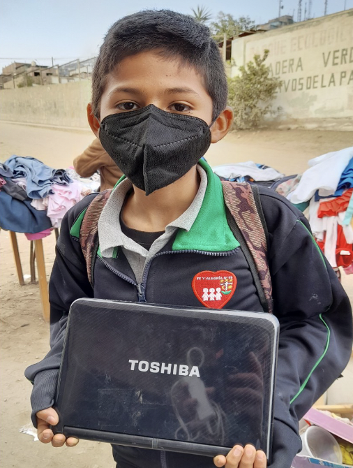 Un jeune garçon péruvien regarde l'objectif en tenant une tablette dans ses mains. Il porte un masque chirurgical.