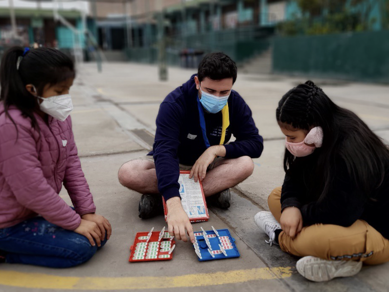 On peut voir ici un volontaire en train de jouer avec deux enfants péruviens dans la cour de l'école.